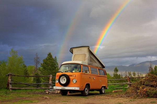 Orange vintage camper van with pop-up roof parked outdoors under a double rainbow
