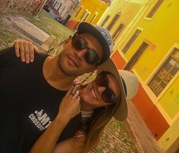 Pictured: man and woman smiling wearing hats and sunglasses in alleyway
