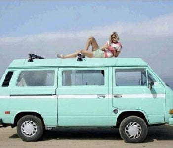 Pictured: sea foam colored camper van outside with woman lounging on top