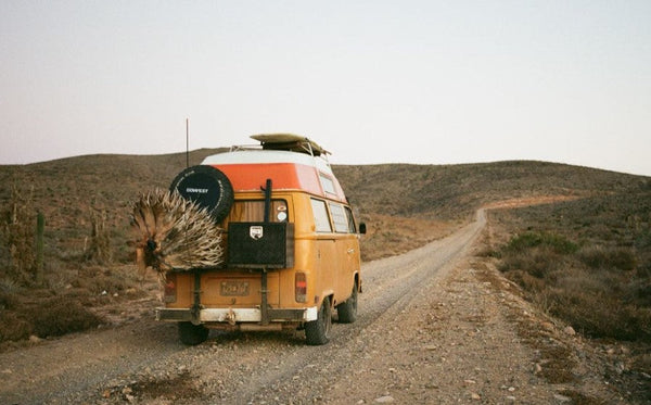 Vintage yellow camper van with roof storage on dirt road in desert landscape