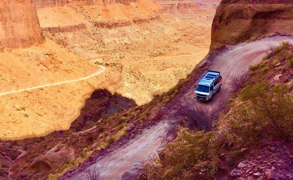 Camper van driving on a rugged desert canyon road with red rock cliffs and scenic landscape
