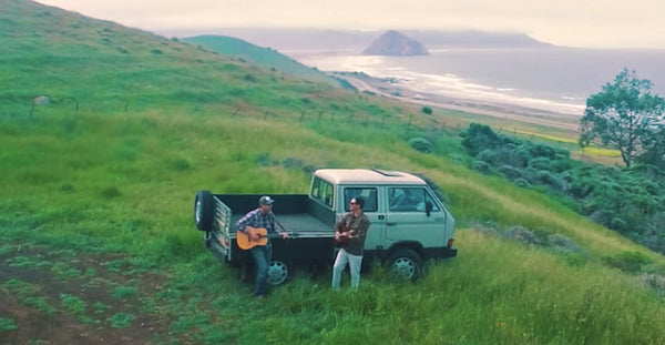 Pictured: the two Driftwood Brothers playing guitar outside next to a camper van
