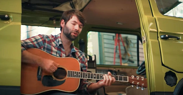 Pictured: Joel Van Horne standing with a guitar in front of a green camper van