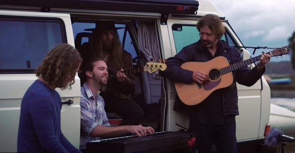 Pictured: Four people playing various instruments in front of a white camper van