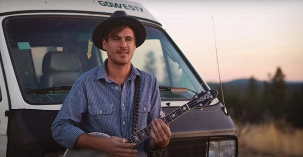 Pictured: A man with a banjo and dog standing next to a white van 