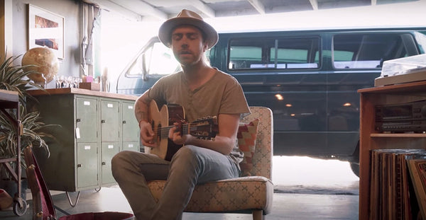Man playing acoustic guitar indoors, vintage van parked in background, cozy home setting