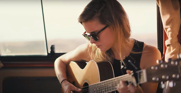 Woman wearing sunglasses playing acoustic guitar inside a camper van