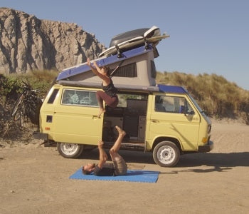 Pictured: couple doing acroyoga in desert setting with yellow camper van behind them