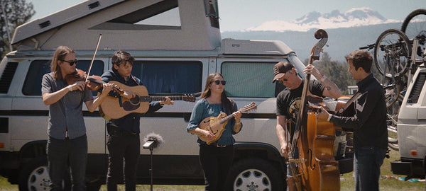 Outdoor band playing string instruments in front of a camper van and mountains