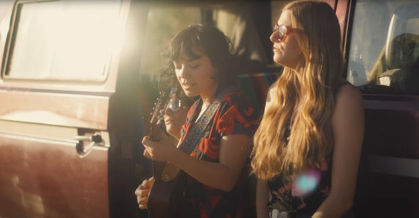 Two women with guitar relaxing by vintage camper van at sunset
