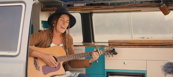 Woman playing acoustic guitar inside a camper van interior with wood accents