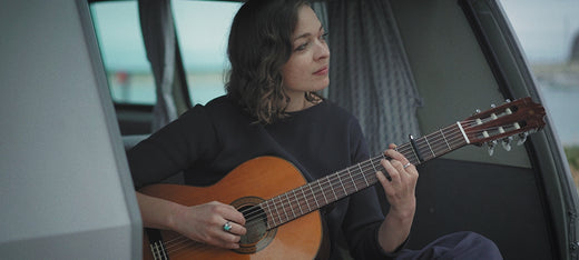 Woman playing acoustic guitar inside a camper van with open door and curtains