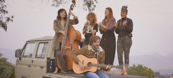 Group of people playing music and singing on a classic camper van roof outdoors