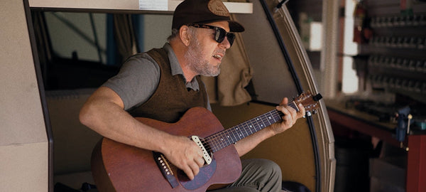 Man wearing sunglasses and cap plays acoustic guitar inside camper van