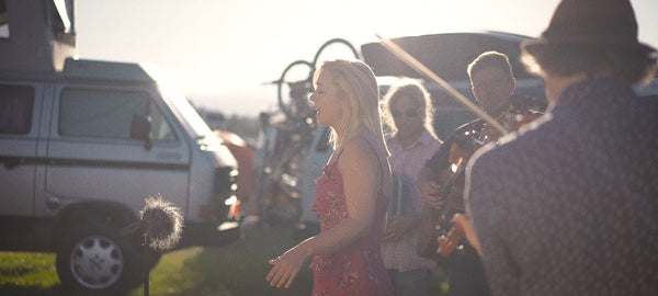 Musicians performing outdoors near a camper van with bicycles in the background, sunny day.