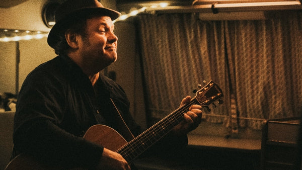 Man playing acoustic guitar inside cozy camper van with string lights