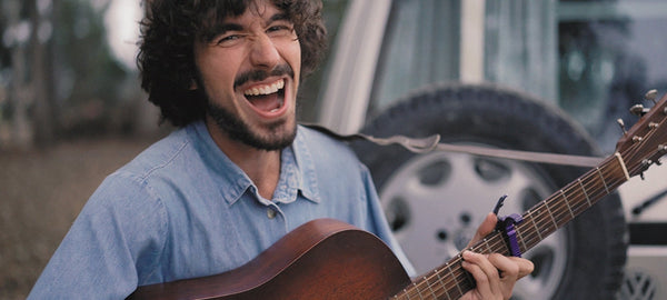 Smiling man playing acoustic guitar outdoors near camper van