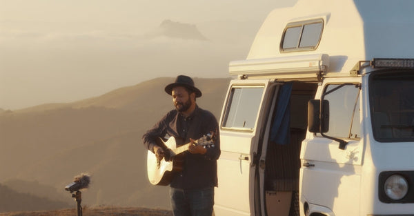 Man playing guitar beside camper van at sunset in scenic mountain landscape