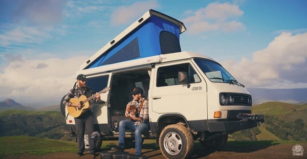 Pictured: Two guitarists play in front of a white Westfalia van outside