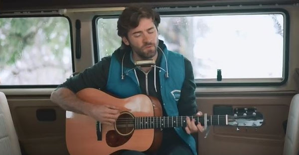 Pictured: John Craigie  playing guitar while sitting in a camper van