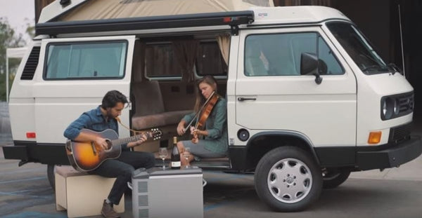 Pictured: Zach Torres plays the guitar next to a woman playing the viola while sitting in a white camper van