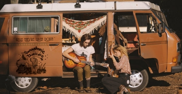 Pictured: A couple sits holding guitars by an open van